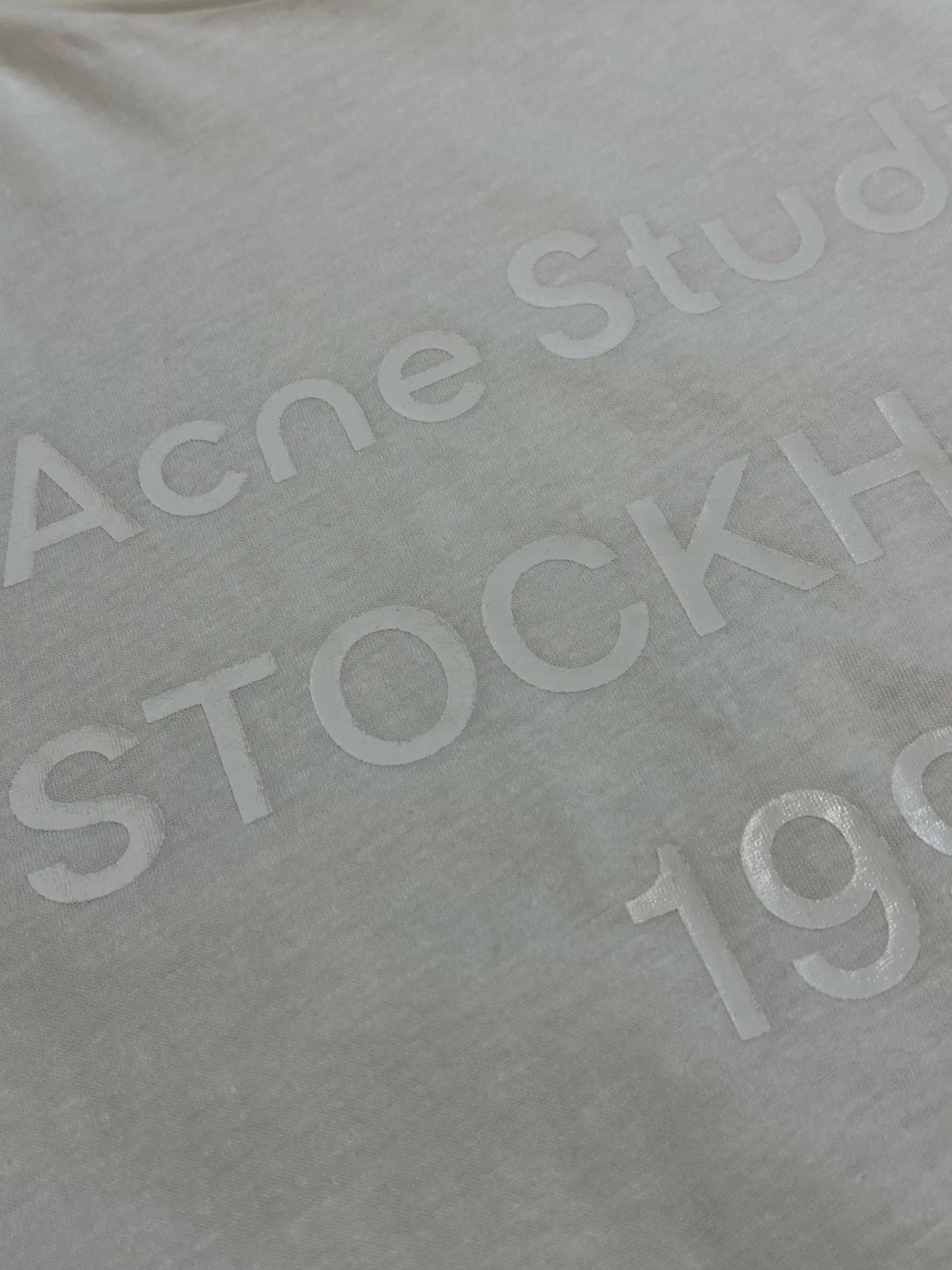 Ac White Letter Round Neck Short Sleeve The fabric is made of 32-count cotton and linen blended plain knitting, with a ratio of 85% cotton and 15% linen fiber. The weight is only 145g/m²; the ribbed neckline is made of Same Style cotton and linen blended yarn, 145g/m², to ensure a unified texture of the entire piece. The collision of the natural rough base and the industrial spraying process creates a natural irregular texture and an extremely light and breathable wearing experience. Cotton provides a skin-friendly and soft foundation, while linen introduces natural roughness and knotted particles, giving the fabric surface an irregular texture. The addition of hemp fiber makes the fabric have excellent moisture absorption and perspiration properties, while also bringing a natural micro-wrinkle texture and dry touch. After the fabric is piece-dyed, the dye evenly penetrates into the fiber, showing full color fastness and soft matte color, providing a uniform base for subsequent inkjet printing. The front is decorated with logo printing. The printing uses a double-layer printing process of environmentally friendly elastic glue and varnish, which takes into account the concept of environmental protection, wearing comfort and visual expression. The bottom layer uses environmentally friendly elastic glue, with water-based environmentally friendly resin as the base material. The color paste is scraped onto the surface of the fabric through a high-mesh screen. After drying and solidifying at high temperature, a soft and highly elastic continuous adhesive film is formed. The printed film can stretch and retract with the fabric. Even if it is covered with a large area of ​​pattern, it is still breathable and does not feel tight when wearing it. The surface layer is accurately overprinted with transparent varnish, creating a high-gloss effect in specific areas. This layer of varnish not only significantly improves the color contrast of the pattern, but also creates a local wet and bright visual and tactile contrast, making ordinary printing instantly gain three-dimensional layers and glossy texture. At the same time, the smooth surface layer also enhances Wear-Resistant and wash-resistant properties. This T-shirt is defined as a neutral style, casual fit, and hip length; its style logic pursues a genderless sense of wrapping and extended proportions. The key point is that the dress is hip-length, not only to cover the buttocks, but also to create a lazy, flowing silhouette by utilizing the lengthened body and the drape of the fabric. In terms of process execution, the side seams need to maintain a straight hem to prevent the long body from looking like a straight bucket. Taken as a whole, it's a hybrid that combines the functional details of workwear with the relaxed feel of high fashion. size：xs s m l